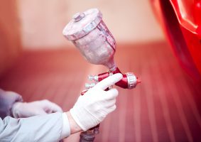 Worker painting a red car in paiting booth using professional tools